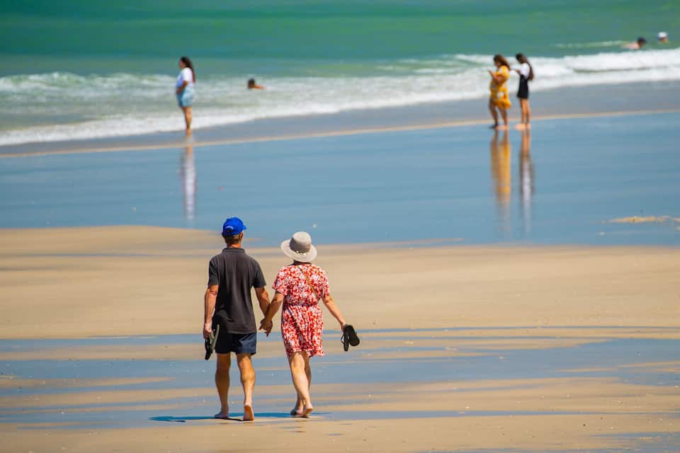 Una coppia che cammina su una spiaggia sabbiosa, con le onde sullo sfondo.