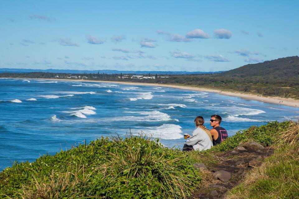Un paisaje costero con playa, olas del océano y un fondo montañoso.