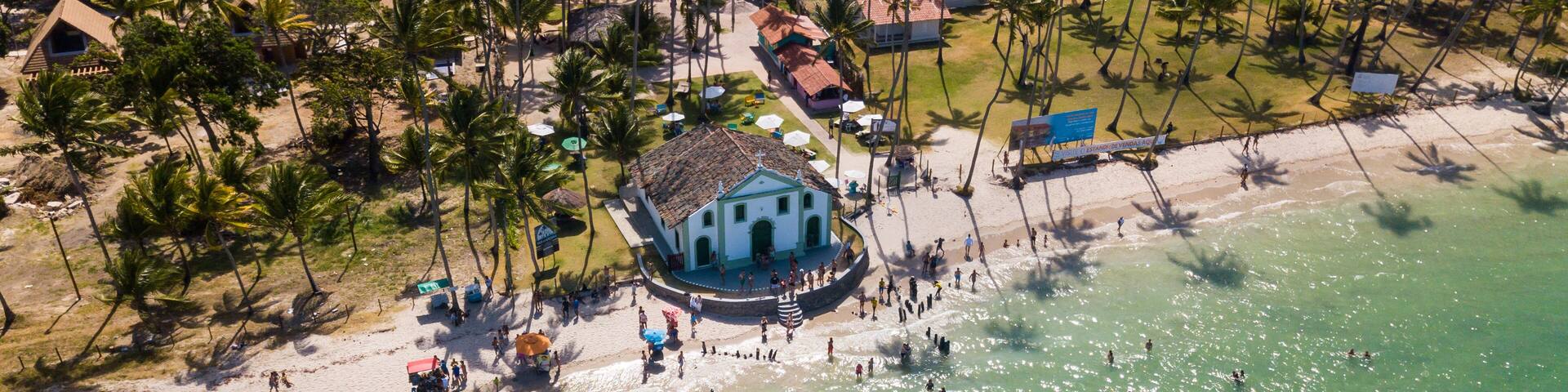 A beach with a central building surrounded by palm trees and people.