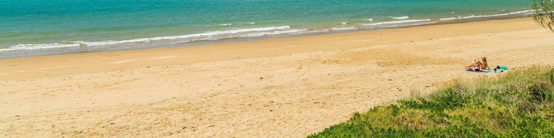 A beach with clear turquoise water, sandy shore, and two small islands in the distance.
