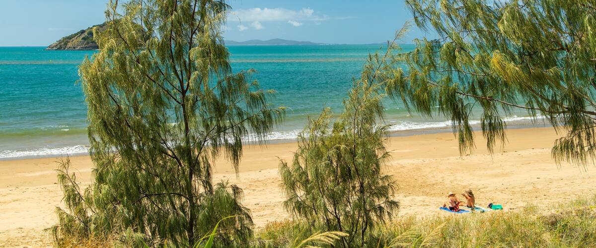 A beach with clear turquoise water, sandy shore, and green trees.