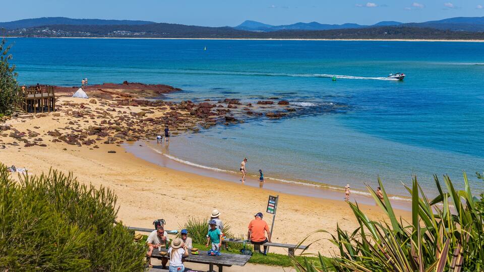 A beach with clear blue water, rocky shoreline, and people enjoying the area.