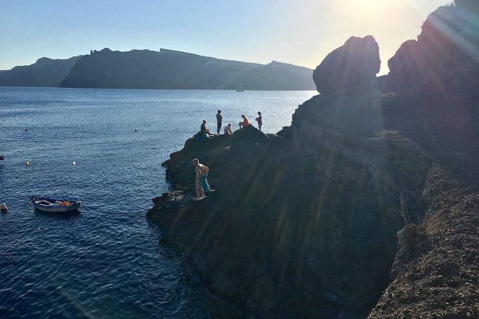 A rocky coastline with people standing on the edge, overlooking the sea.