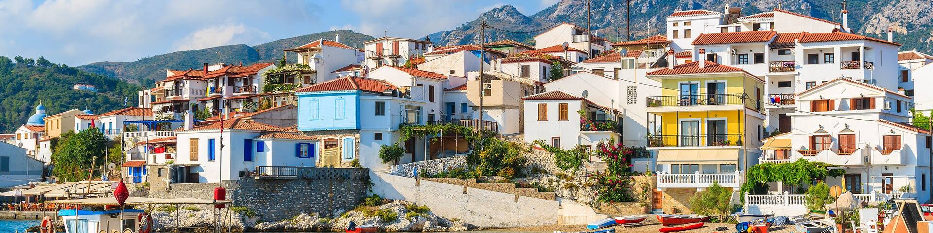 Un pueblo costero con edificios coloridos, barcos amarrados en el agua y montañas al fondo.