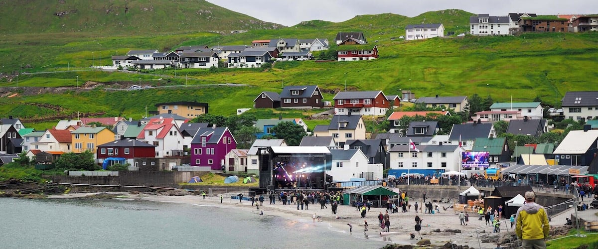 A coastal town with colorful houses, a rocky shoreline, and a crowd near a stage.