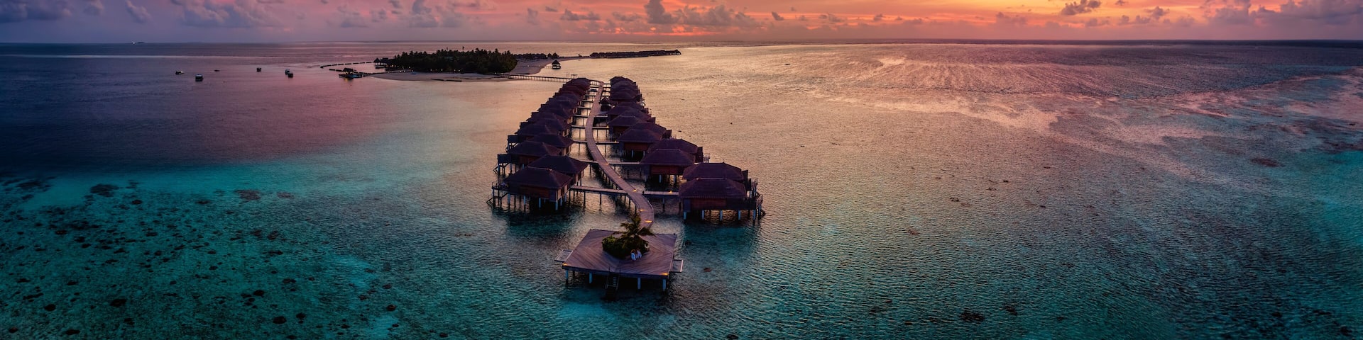 Aerial panorama of a tropical paradise island in the Maldives, Indian Ocean, with water lodges over the turquoise reef during sunset time