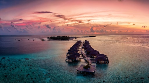 Aerial panorama of a tropical paradise island in the Maldives, Indian Ocean, with water lodges over the turquoise reef during sunset time