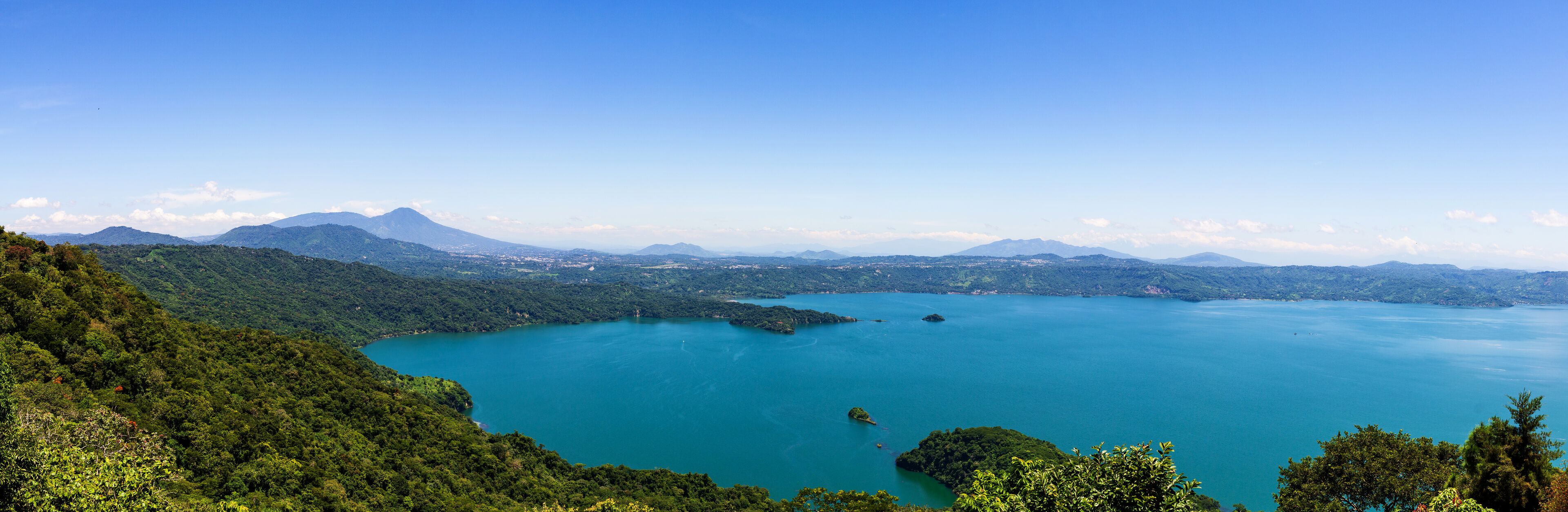 A large lake surrounded by lush green mountains and a clear blue sky.