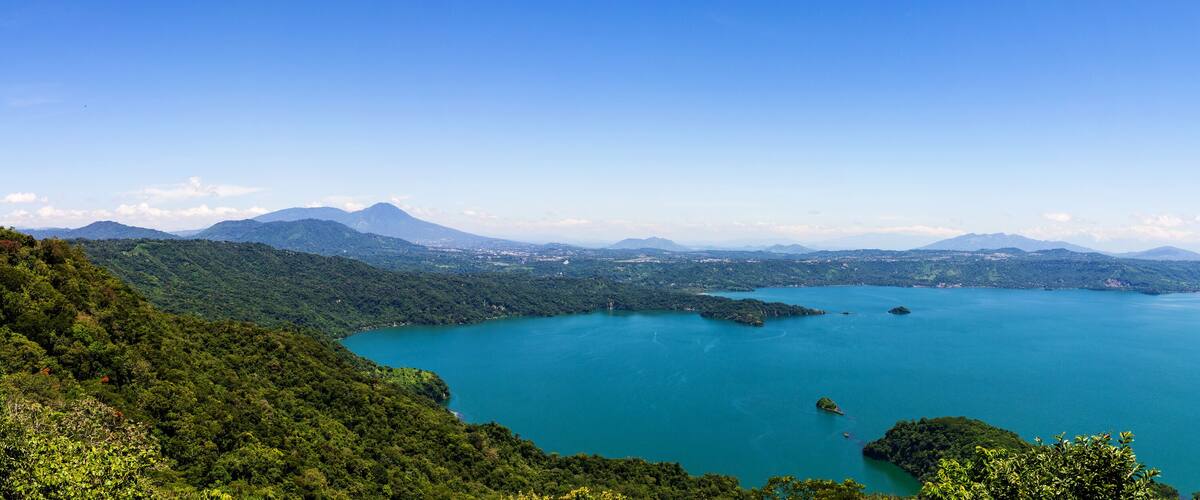 A large lake surrounded by lush green mountains and a clear blue sky.