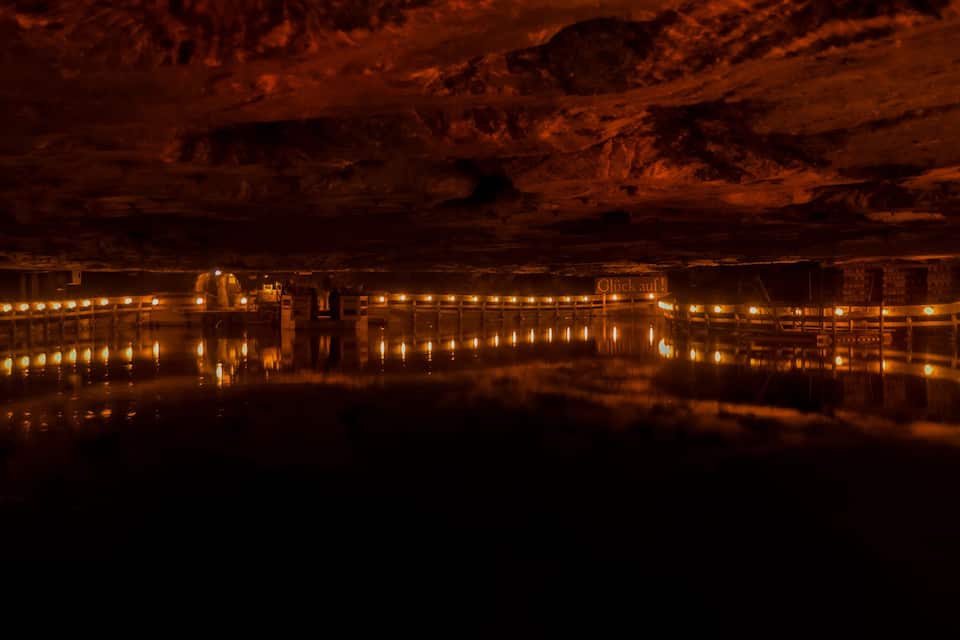 A nighttime view of a cave with illuminated structures and a reflective water surface.