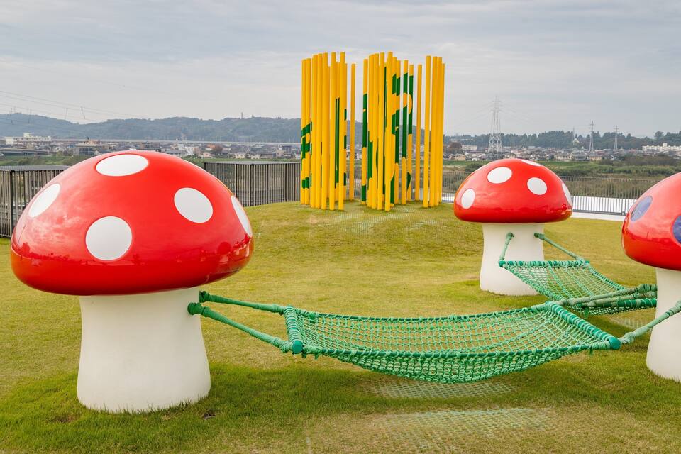 Un parque con estructuras en forma de hongo y un puente colgante verde.