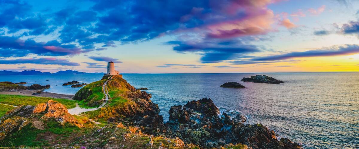 A coastal landscape with a lighthouse, rocky outcrops, and a sunset over the ocean.