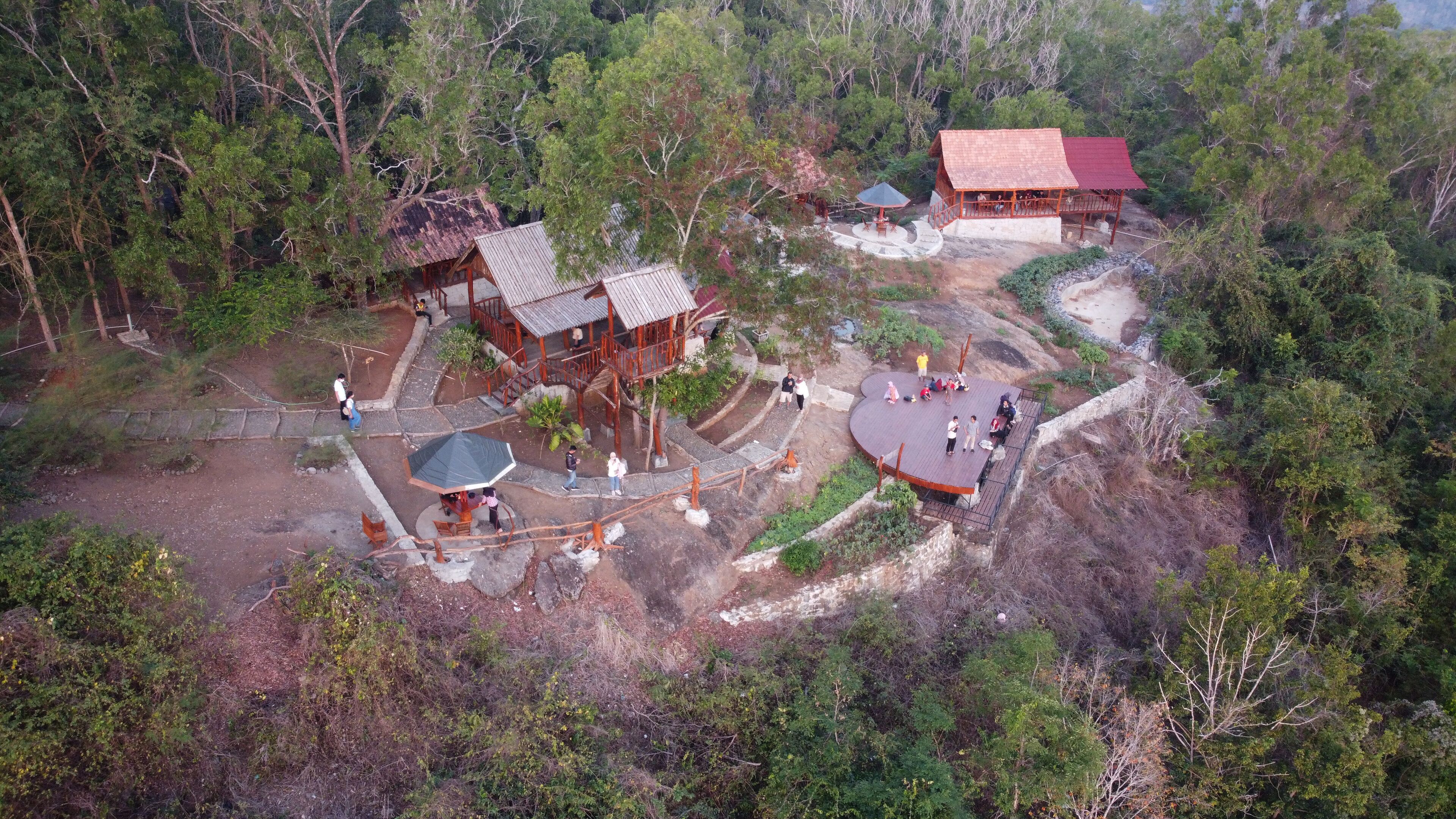 A forested area with wooden structures and a red-roofed building.