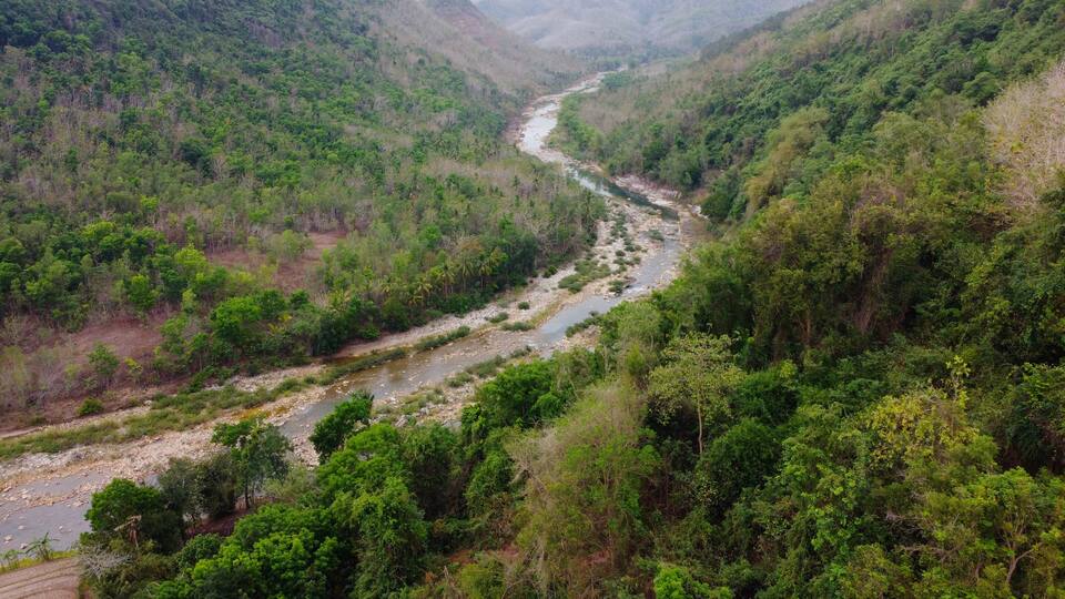 A river winding through a lush valley with dense greenery and hills in the background.