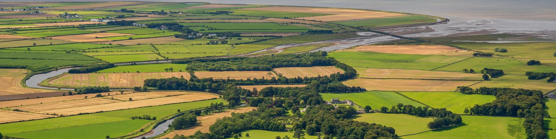 A coastal landscape with fields, a river, and a body of water.