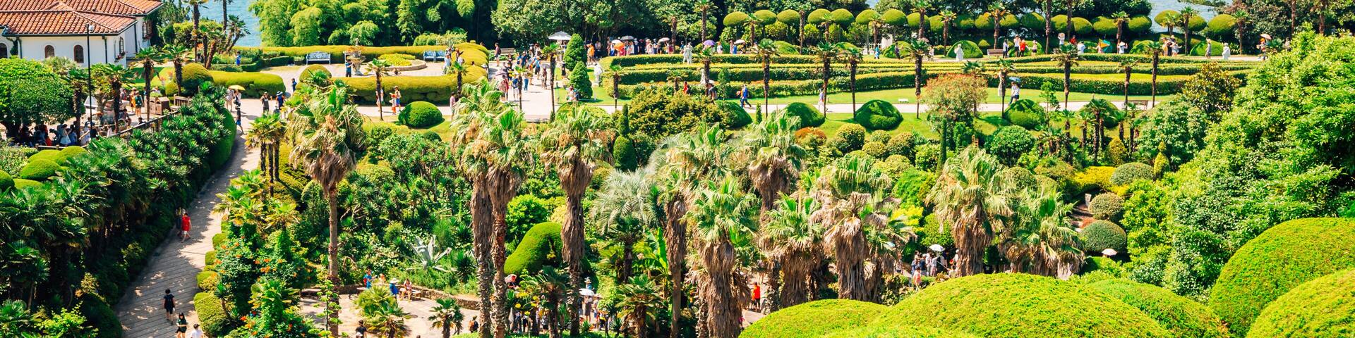 A coastal garden with manicured hedges, palm trees, and a view of the sea and distant islands.