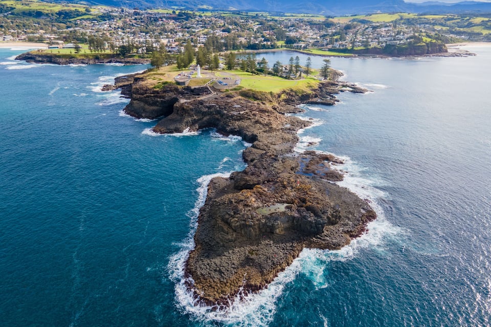 A coastal town with a prominent lighthouse, rocky shoreline, and a bay with surrounding greenery.