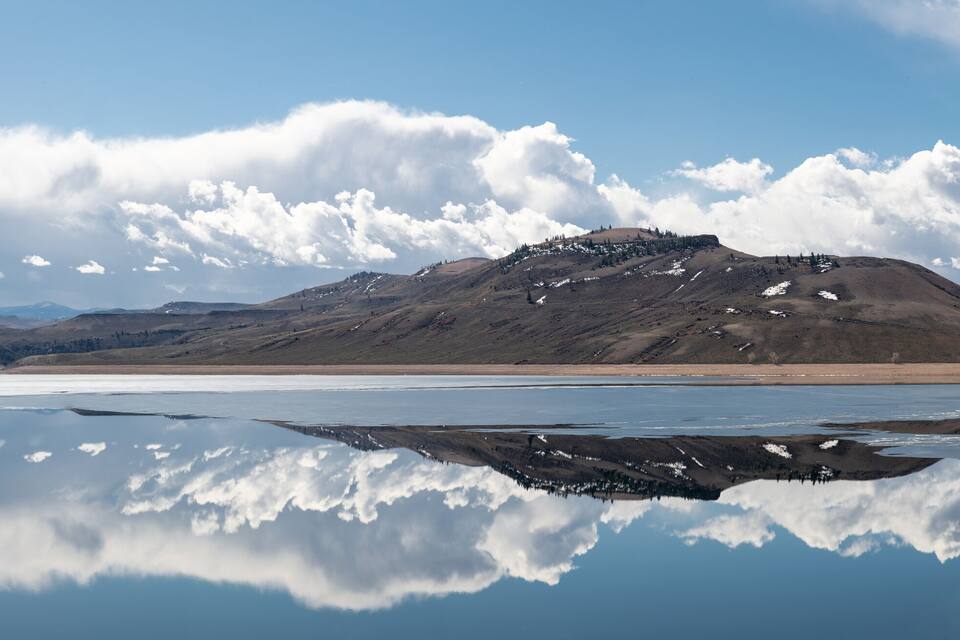 A calm lake reflecting clouds and mountains.