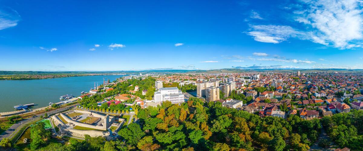 A panoramic view of a city with a river, a large white building, and surrounding greenery.