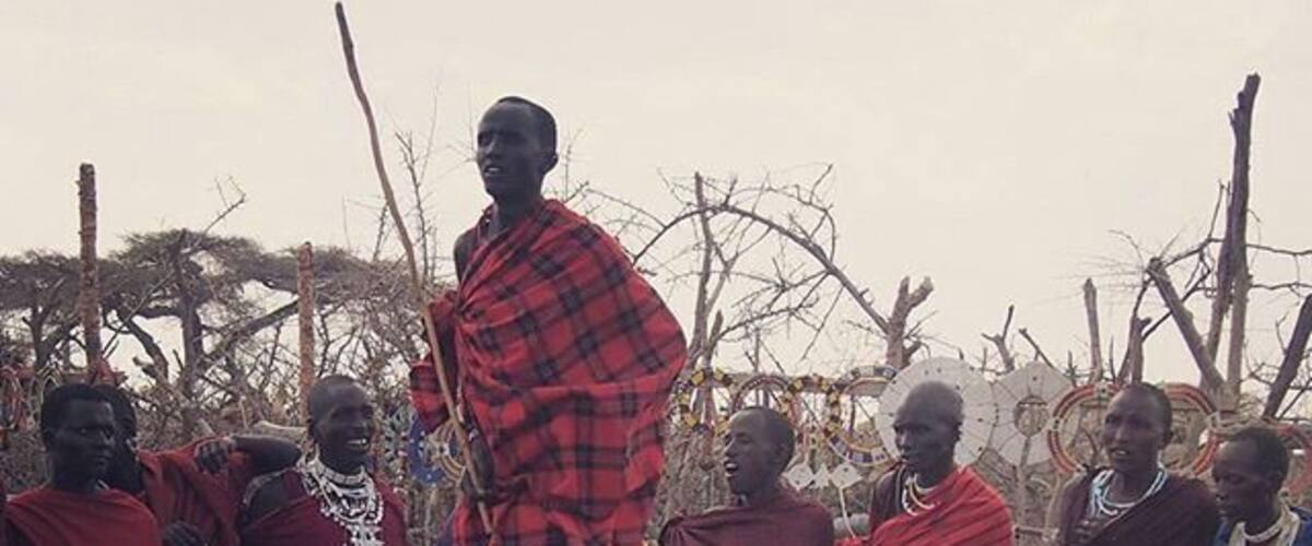 A group of people in traditional attire standing in a natural setting with sparse trees.