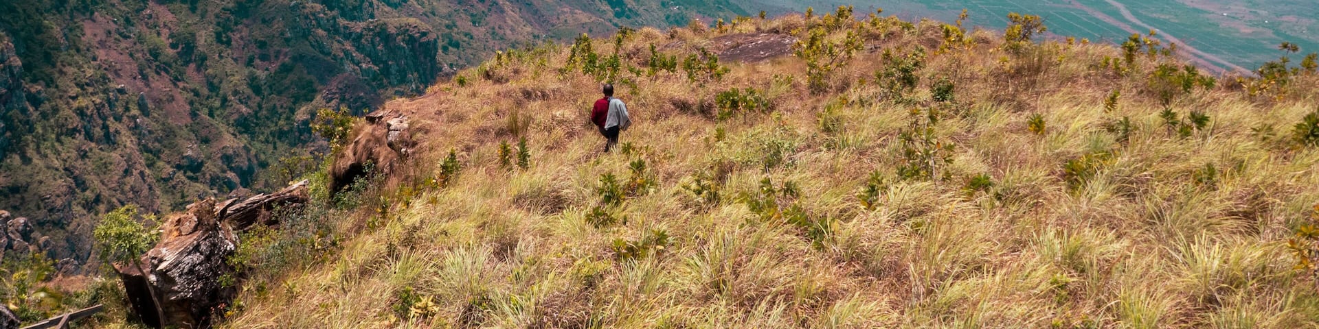 A hiker on a grassy hill with a view of distant mountains and valleys.