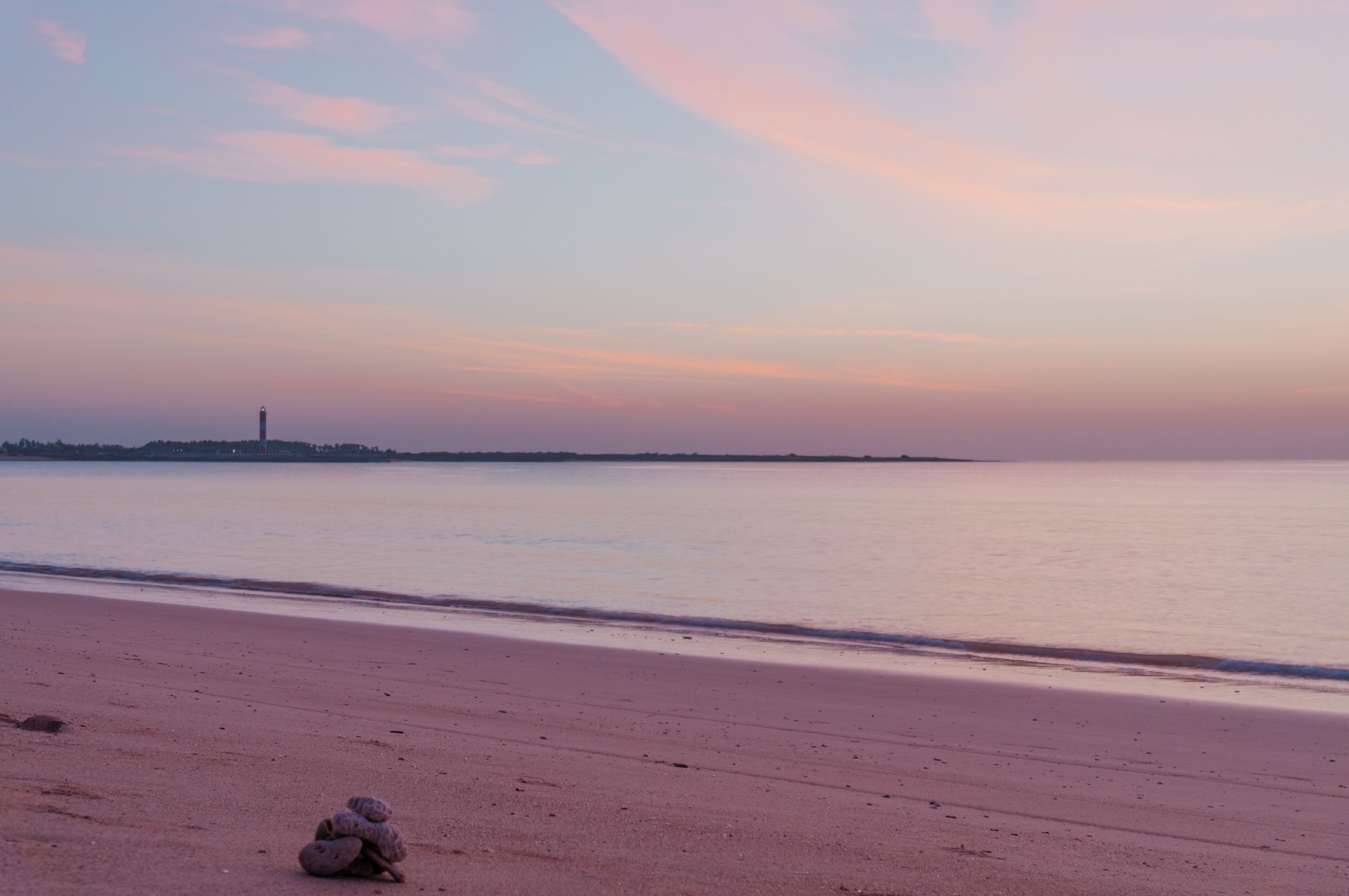 Sunset at Shivrajpur beach dwarka gujarat. Shows the very beauitful beach with its beautiful sand, waves lapping the shore, clouds and the lighthouse in the distance. Light changes from golden to cool
