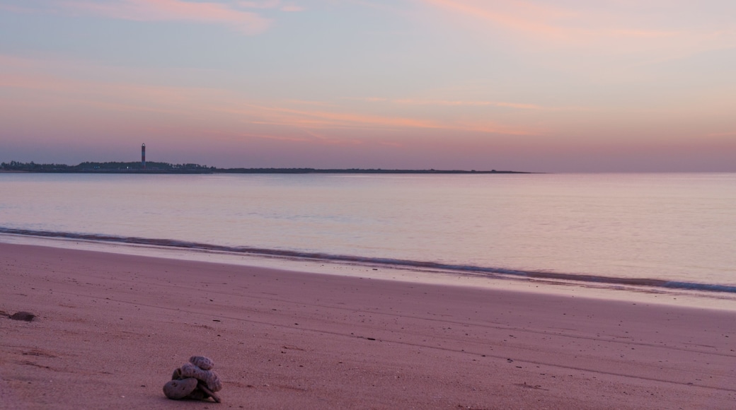 Sunset at Shivrajpur beach dwarka gujarat. Shows the very beauitful beach with its beautiful sand, waves lapping the shore, clouds and the lighthouse in the distance. Light changes from golden to cool