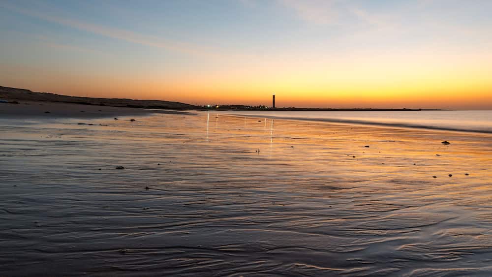A beach at sunset with a distant tower.