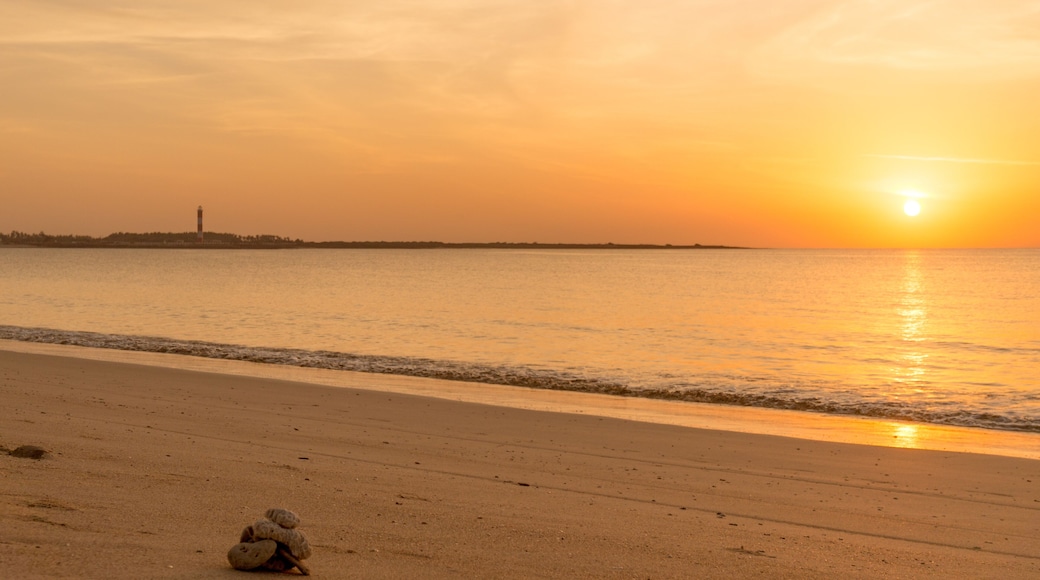 Sunset at Shivrajpur beach dwarka gujarat. Shows the very beauitful beach with its beautiful sand, waves lapping the shore, clouds and the lighthouse in the distance. Light changes from golden to cool
