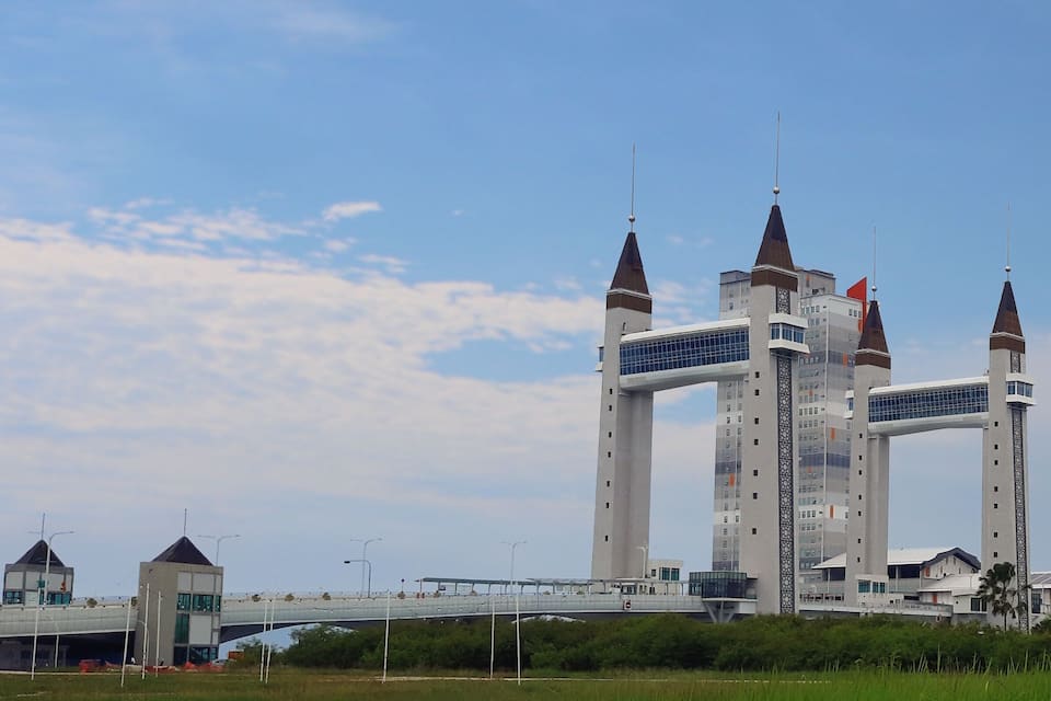 A modern building with three tall towers and a bridge in the foreground.
