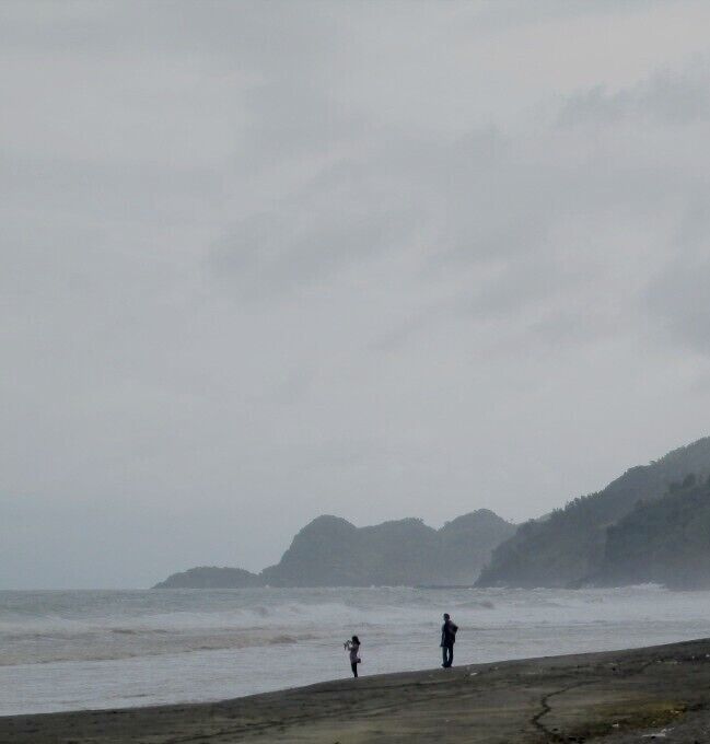 A beach with rough waves and a hilly landscape in the background.