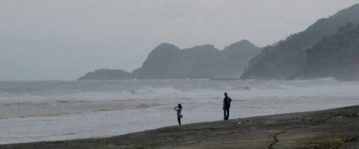 A beach with rough waves and a hilly landscape in the background.