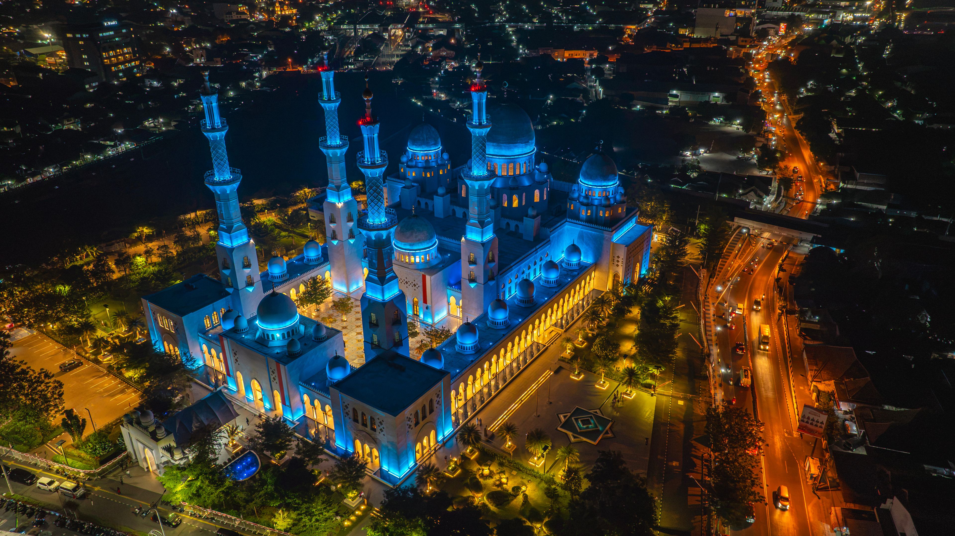 A large mosque with multiple domes and minarets, surrounded by a well-lit courtyard and adjacent roads.