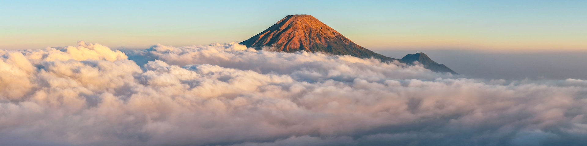 A mountain with a conical shape, surrounded by a sea of clouds.
