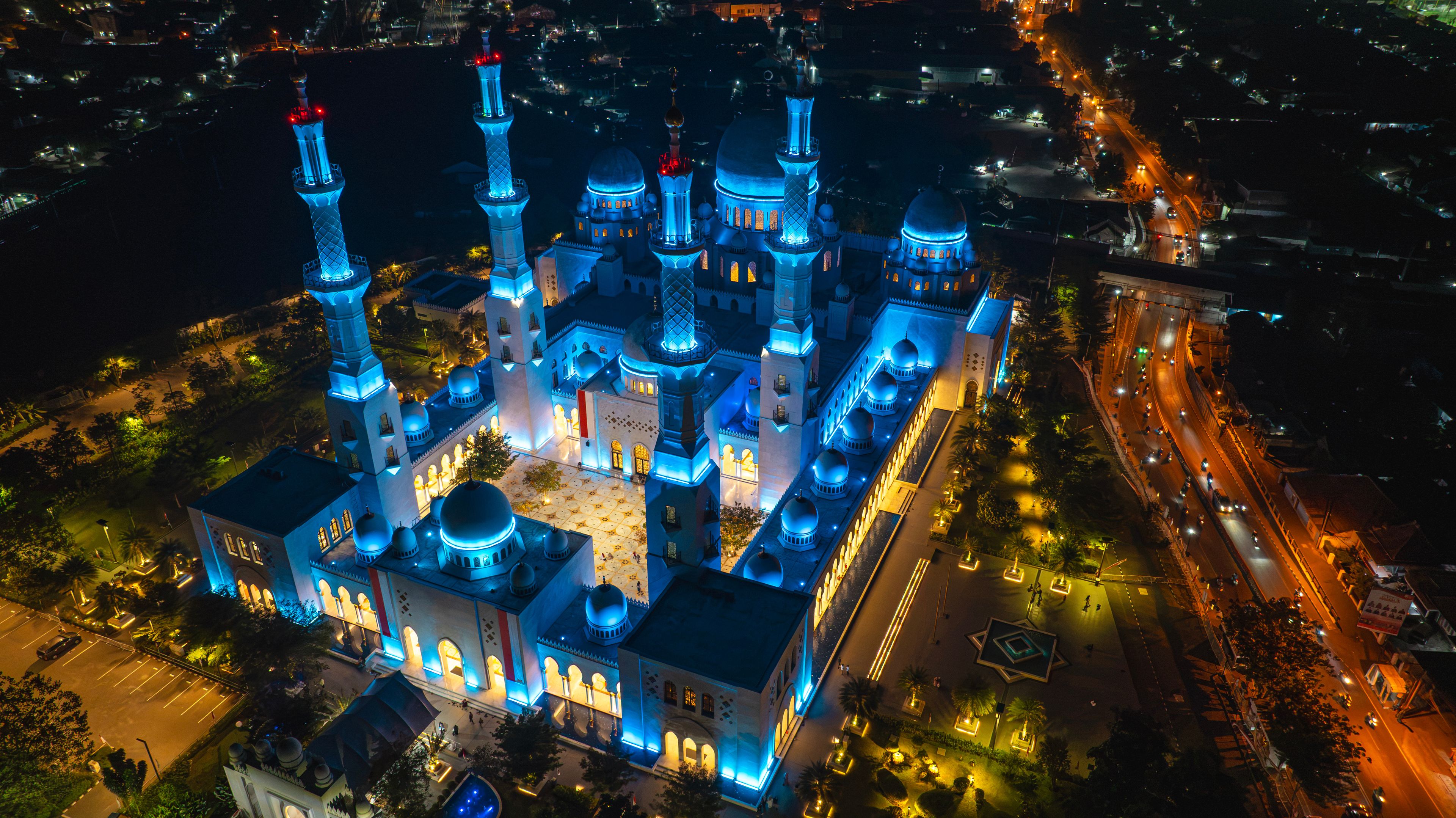 A large, illuminated mosque with multiple domes and minarets, surrounded by a cityscape at night.