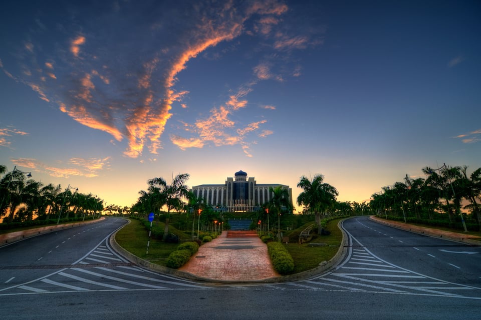 A grand building with a dome, surrounded by palm trees and a curved road leading to it.