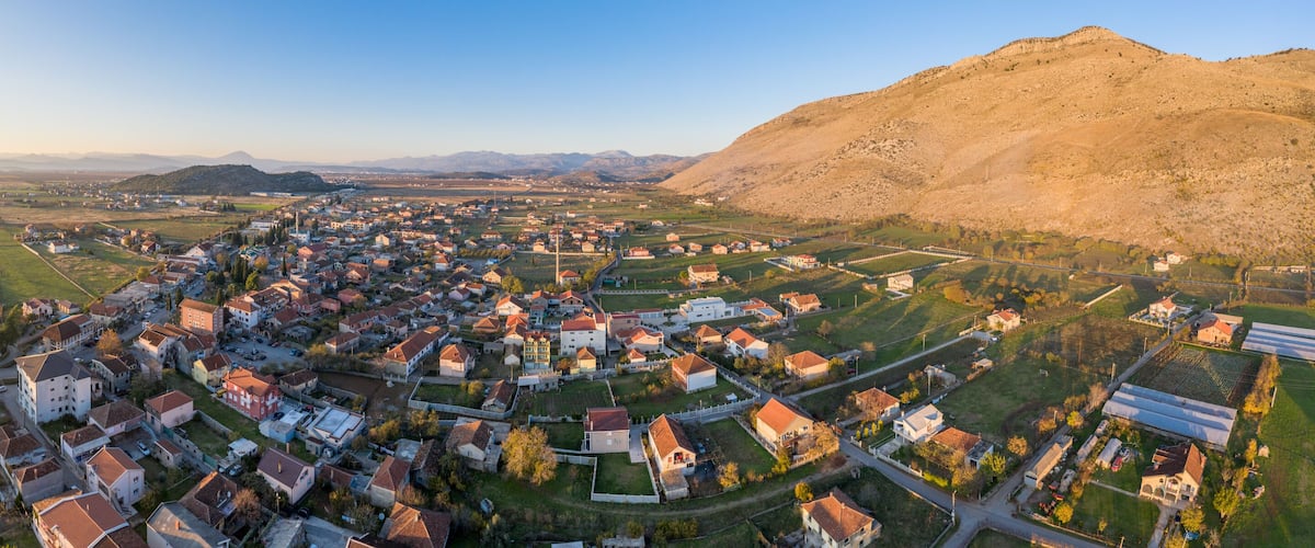 An aerial view of a town with a prominent church, rolling hills, and a mountain in the background.