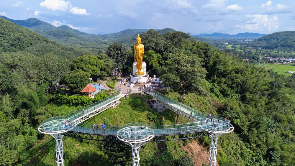 A golden statue surrounded by lush greenery and a glass bridge.