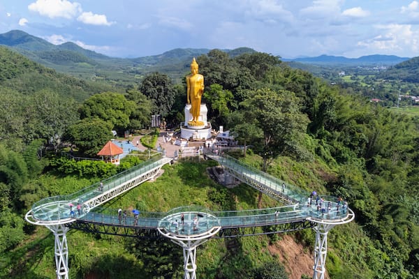 A golden statue surrounded by lush greenery and a glass bridge.