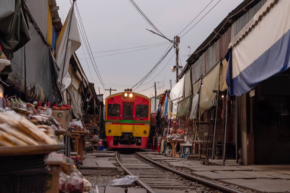 Um trem nos trilhos em uma rua urbana estreita, com edifícios em ambos os lados.