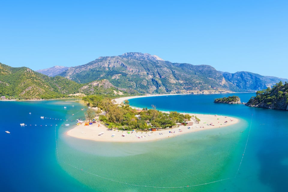 A coastal landscape with a small island, clear turquoise waters, and mountainous terrain.