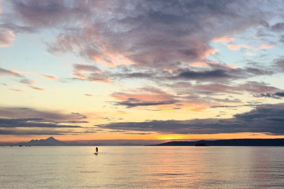 A sunset over a calm sea with a silhouette of a person paddleboarding.