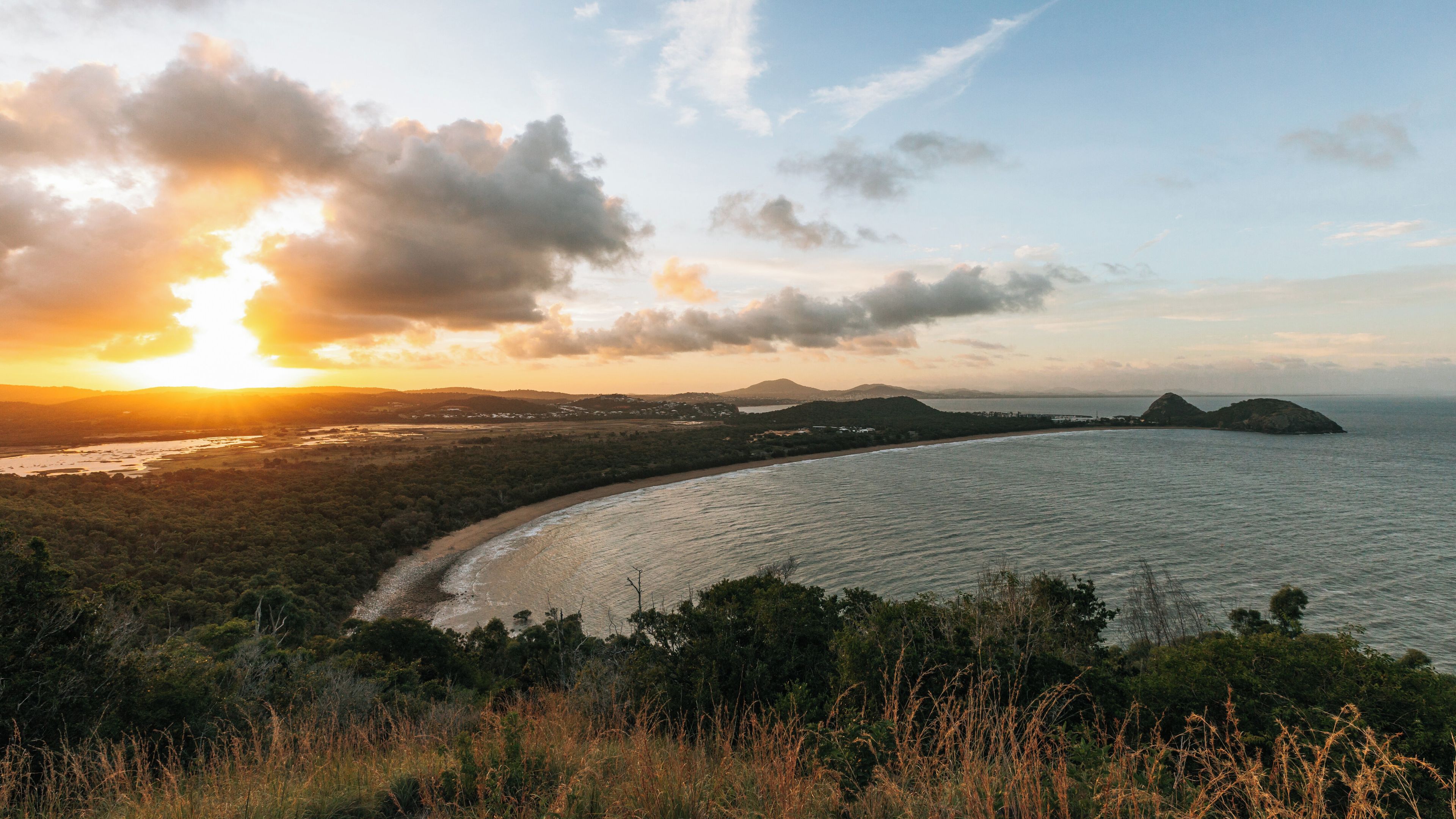 A coastal landscape with a river curving through a forested area, leading to a beach with waves.