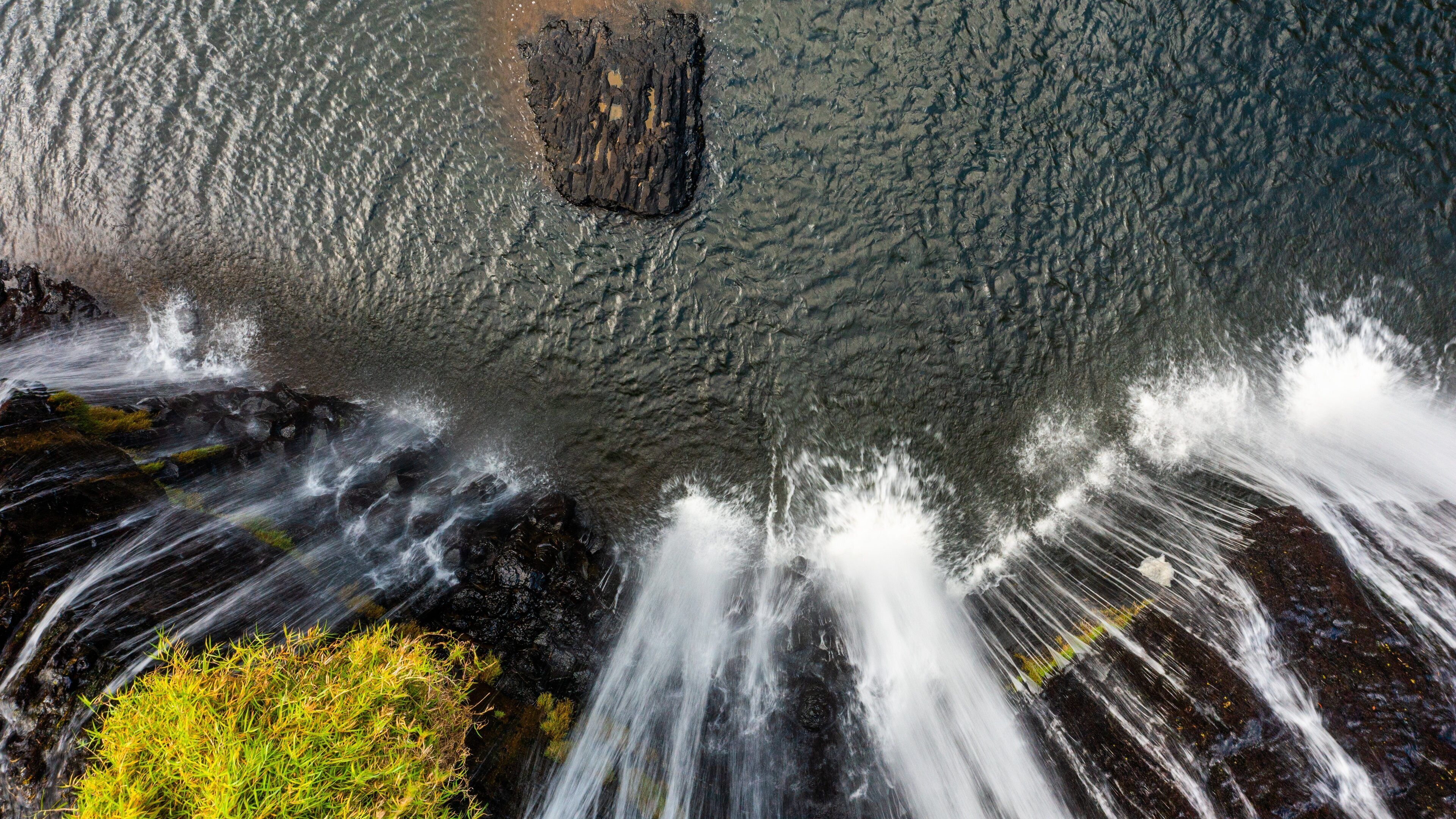 A waterfall cascading over rocks with a small green plant at the base.