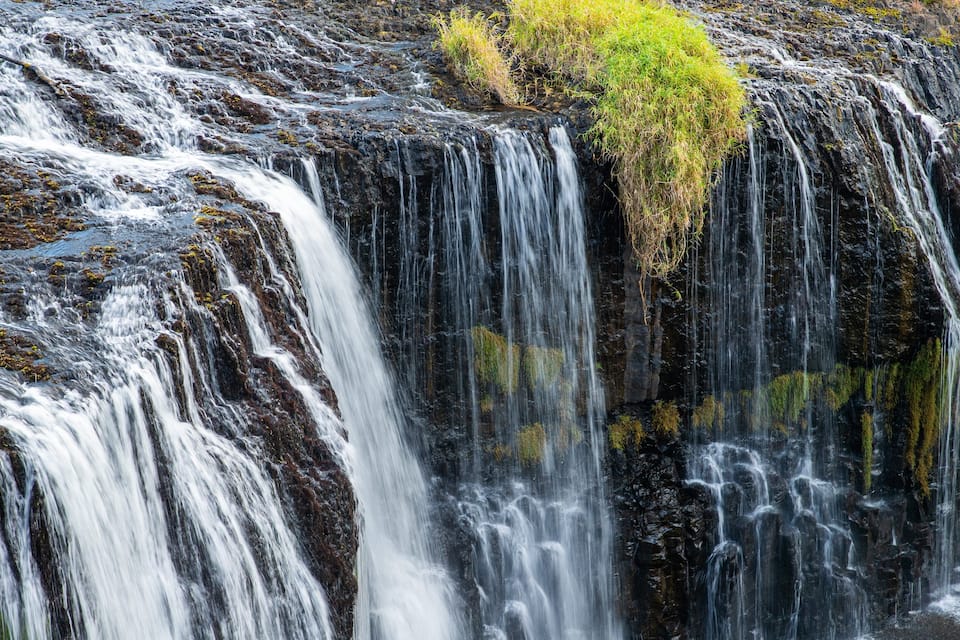 Una cascada se precipita sobre rocas oscuras cubiertas de musgo.