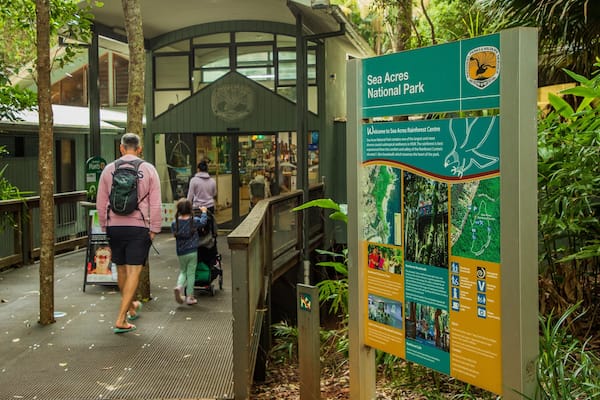 A wooden boardwalk in a rainforest, with a sign for Sea Acres National Park and Rainforest Centre.