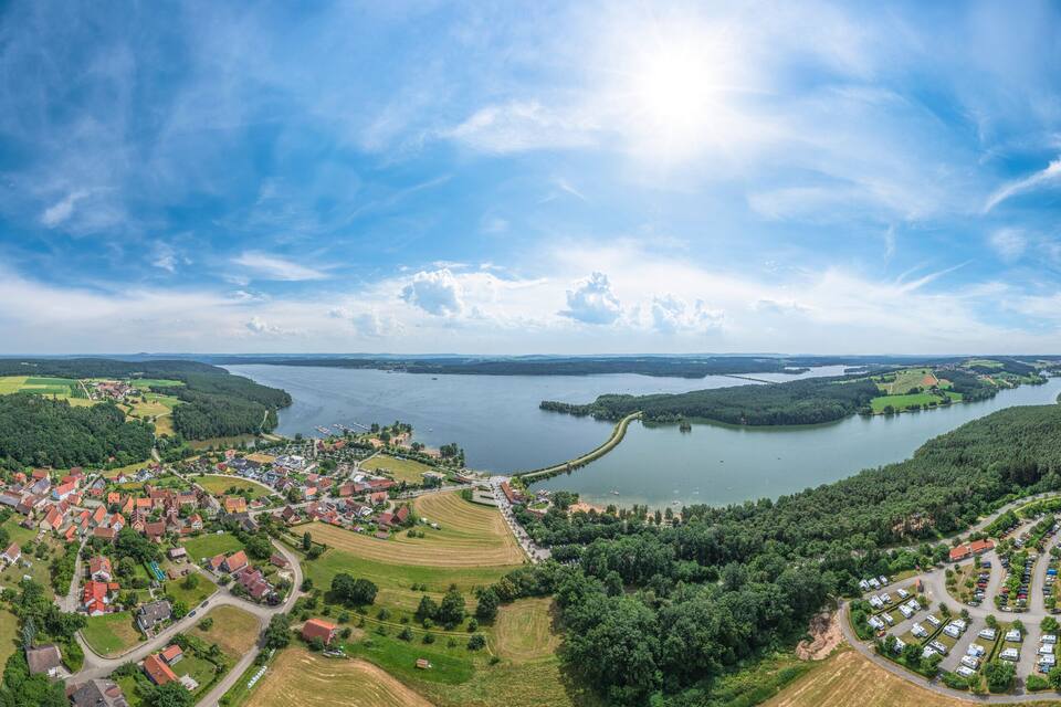 A panoramic view of a lakeside village with houses, fields, and a winding road.