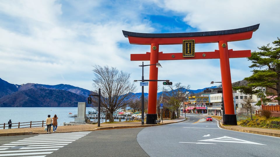 A red torii gate at a waterfront with mountains in the background.