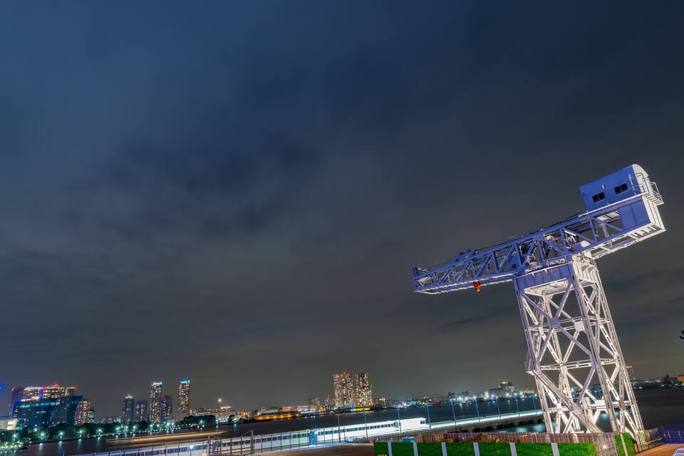 A nighttime cityscape with a prominent crane structure and illuminated buildings.