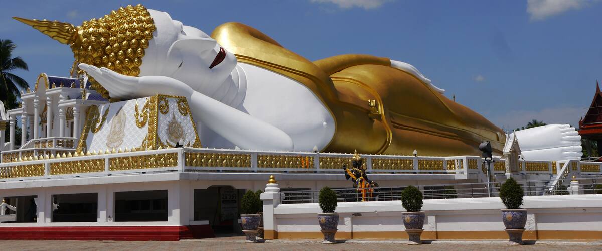 A large white and gold reclining Buddha statue with intricate detailing, set against a clear blue sky.